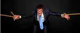 Constrain (V)  - Compel or force (someone) to follow a particular course of action. <strong> (विवश/मजबूर) </strong>